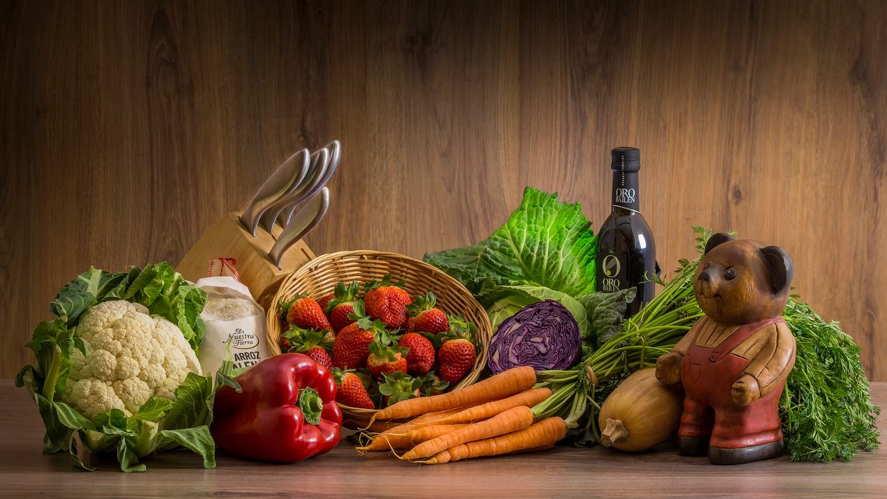 hero-img-02 Arrangement of fresh vegetables and fruits on a wooden table with kitchen essentials.