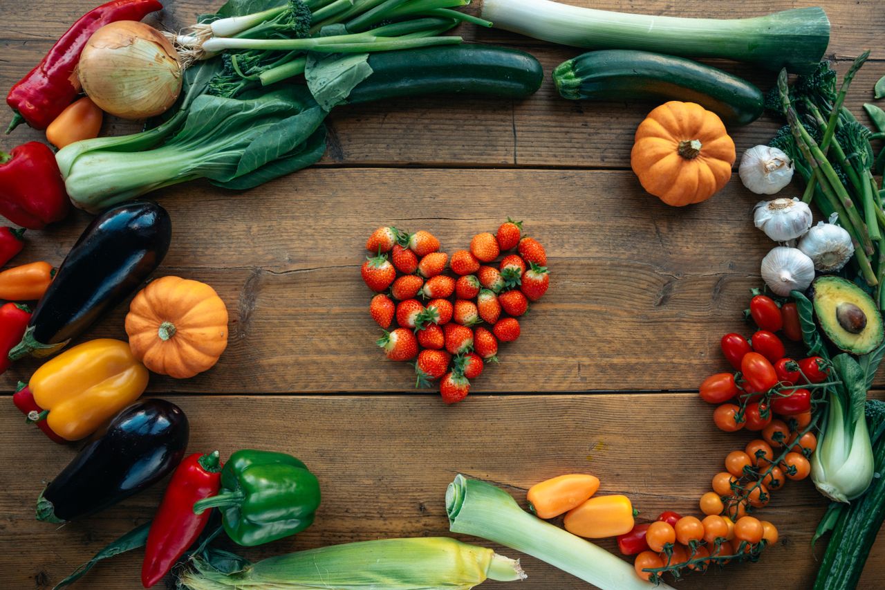 services-01 Vibrant fruits and vegetables arranged heart-shaped on a wooden surface, top view.
